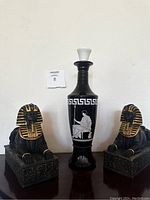 Front view of black and white Roman motif Jim Beam decanter with two painted sphinx figurine boxes on each side.