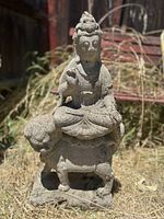 Front view of the vintage stone statue showing Asian Buddha seated on Foo Dog base outdoors on grass.