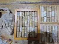 Top view of three framed cork trivets arranged on wooden surface, with a mesh bag holding extra corks positioned nearby. Larger rectangular trivet and two smaller square trivets visible with corks arranged in rows inside natural wood frames.