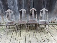 Set of four vintage solid wooden chairs shown from front against wood background.