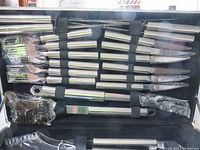 Inside view of aluminum case showing many stainless steel barbecue forks, knives, and knives all secured with black elastic straps.