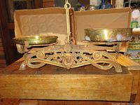 Front view of the balance scale showing the iron body with decorative scrolling and brass trays on either side.