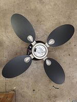 Top view of ceiling fan showing four black oval blades with silver accent near attachment and central light fixture missing its cover.