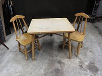 Photo of square wooden children's table with two matching chairs beside it, showing usage wear and paint chipping.