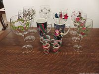 Photo showing 4 large and 4 smaller Christmas glasses, 2 large mugs, 2 small mugs, 2 candy cane shot glasses, 4 small utensils, and assorted swizzle sticks.