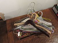 Assortment of wooden, wire, and plastic clothes hangers stacked on a table, showing various styles and colors.