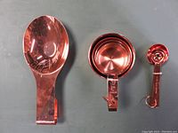 Set photo showing copper-colored spoon holder, four measuring cups nested, and four measuring spoons grouped separately.