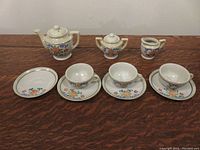 Photo showing miniature porcelain tea set with cups, saucers, teapot, cream and sugar holders arranged in row