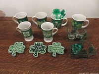 Photo showing all items neatly arranged: 6 themed mugs in three pair designs, 3 shamrock shaped plates with Irish sayings, 3 clear shot glasses in wire holder, 2 green metal wire baskets, and green shamrock swizzle sticks.