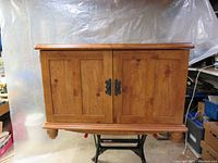 Front view of the wooden TV stereo cabinet showing closed double panel doors with black metal handles, natural wood finish and rounded base.