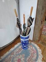 Umbrella stand with three umbrellas placed inside, showing wood floor and partial surrounding area.
