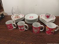 All items including heart-shaped plates, round plates, mugs, and glass snifter shown together on table.