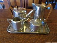 Front angle showing the full set on the tray with coffee pot, tea pot, creamer, and sugar bowl all having a polished metal appearance with wooden handles.
