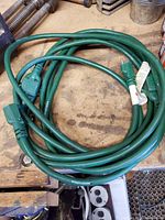 Two green extension cords coiled on a wooden surface showing plugs and outlets.