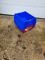 Stacked storage bins showing blue lids and a red base bin with scuff marks and sticker residue on outdoor concrete ground.