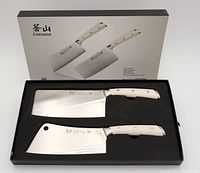 Set of two large and medium meat cleavers with white handles positioned in black foam insert inside box, outer box behind showing product details and brand.