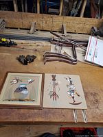 Full view of the two Native American sand art pieces placed on a wooden surface with other workshop items around