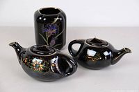Top view of two black ceramic tea pots and one vase showing floral and insect designs