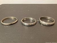 Three silver bracelets displayed on black surface