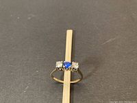 Front view of ring showing round blue center stone flanked by two round diamonds on black background