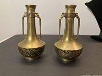 Front view of pair of brass Chinese vases showcasing dragon and floral motifs, narrow necks with handles.