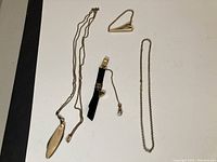 Full view of the 4 antique men's jewelry items including pocket knife pendant necklace, tie clip with chain, and two chain necklaces.