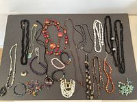 Overview of the variety of beaded jewelry pieces laid out on a dark surface showing multiple necklaces and bracelets.