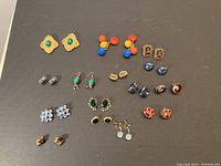 Top down view showing all 16 pairs of earrings arranged in rows on a dark background.