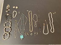 Top view of various pearl jewelry pieces including bracelets, rings, earrings, and necklaces arranged on a black surface