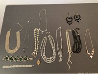 Full display of all vintage costume jewelry items including necklaces, bracelets, earrings and brooch on a dark background