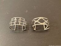 Top view photo showing both sterling silver cuff bracelets with openwork geometric designs on a dark background.
