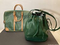 Two green leather bags side by side on a surface. One briefcase-style with tan handles, the other a bucket bag with drawstring closure.