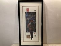 Full view of one framed print showing figure walking barefoot near waterfall, with black frame and white mat including red accents and seals.