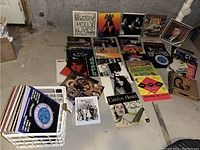 Overview of multiple vinyl LPs laid on concrete floor, including a crate of records and loose album covers.