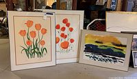 Three framed wall art pieces standing together. Two prints with orange tulips and one abstract watercolor painting.