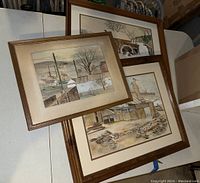 Three framed art pieces by Grace Herley on a table, various rural scenes.