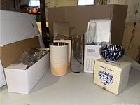 Overview of lot including boxed Eparé champagne flutes, Society6 metal wine chiller, clear glass pitcher, acrylic stemless wine glasses in box, and West Elm indigo bowls boxed