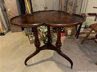 Full view of cloverleaf wooden table showing the distinct cloverleaf top and ornate central legs with casters on feet.