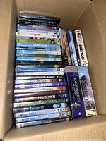 Photo of a large stack of DVDs in a box, showing various movie and documentary titles.