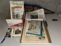 Photo showing box with travel magazine titled 'Britain Aimed at Yankee Visitors', included Britain map, postcards, and vintage newspapers.