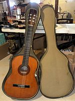 Classical guitar in its open hard shell case, showing the full guitar and case interior, highlighting the wood finish and padding of the case.