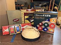 Lot laid out on table: LL Bean Scrabble case, Mah Jongg set box, Minnesota Fats billiard ball box, playing cards, cribbage board, and carved wood musical instrument