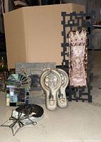 Full view of the lot showing metal and ceramic wall art, pottery candle holders and stained glass pieces against cardboard backdrop on basement floor.