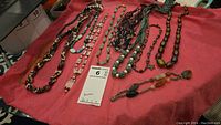 Overview of 11 different costume jewelry necklaces displayed on red fabric, including two tie-on styles and one stretch style with beads.