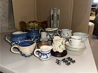 Overview of pottery items including creamers, teacup, saucers, vase on wood base, miniature watering can, and painted wood screen.