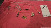 Full view of all jewelry items laid out on a red cloth surface, showing two bracelets, two necklaces, and multiple earrings.