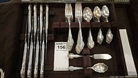 Top down view showing the arrangement of various flatware including forks, spoons and butter utensils, with ornate floral handles.