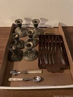 Overall view of the lot showing three pairs of candlesticks (two round base pairs, one square base pair), two mother of pearl spoons, six Revere forks with wooden handles neatly arranged in a tray.