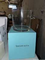 Front angle of clear glass ice bucket on Tiffany blue box, showing one handle and packaging text.
