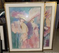 Two framed pastel and watercolor abstract bird paintings with gold highlights, shown leaning against each other in basement setting.